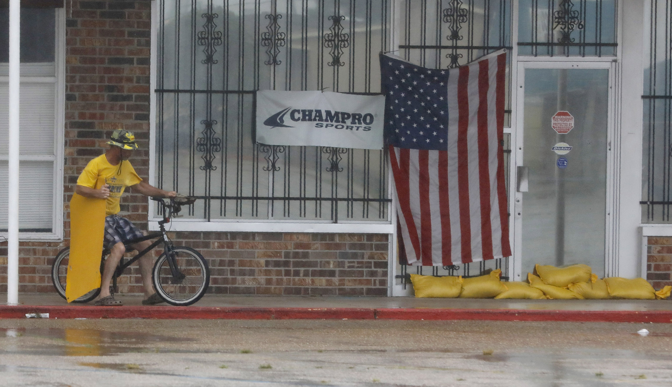 Gordon Helman carries a business poster he picked up from the road as he rides his bike through stiff winds and stinging rain in Morgan City, Louisiana.