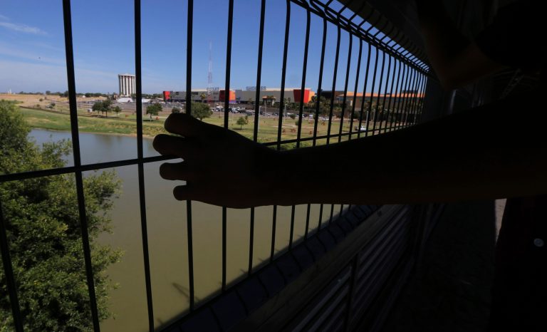 The hand of a youth from Nuevo Laredo rests on the gate as he stops to watch a train pass, above the Rio Grande river on International Bridge 1 Las Americas, a legal port of entry which connects Laredo, Texas in the U.S. with Nuevo Laredo, Mexico, Thursday, July 18, 2019. 