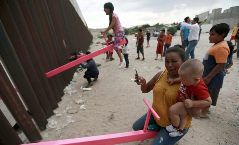 A mother and her baby play on a seesaw installed between the steel fence that divides Mexico from the United States in Ciudad de Juarez, Mexico, Sunday, July 28, 2019. 
