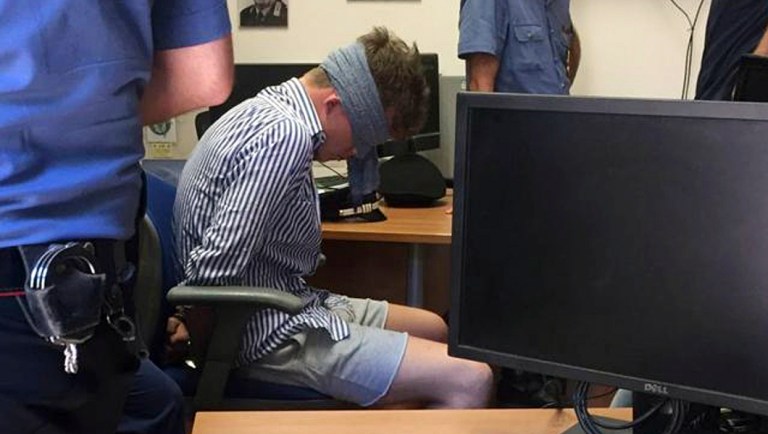 In this photo obtained from Italian Carabinieri, Gabriel Christian Natale-Hjorth sits blindfolded in a police station in Rome on Friday July 26, 2019. Natale-Hjorth, a suspect in the slaying of police officer Deputy Brigadier Mario Cerciello Rega, was blindfolded before he was interrogated in Rome, an Italian police commander said Sunday July 28 after the emergence of a photo showing the young tourist restrained with handcuffs and with his head bowed. Natale-Hjorth and another suspect from California, 19-year-old Finnegan Lee Elder remain jailed, while the murdered police officer Mario Cerciello Rega is to be buried in southern Italy on Monday. (Italian Carabinieri via AP)