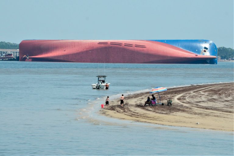 People are shown on Jekyll Island's Driftwood Beach as the Golden Ray cargo ship is capsized in the background, off the Georgia coast, Sunday, Sept. 8, 2019.