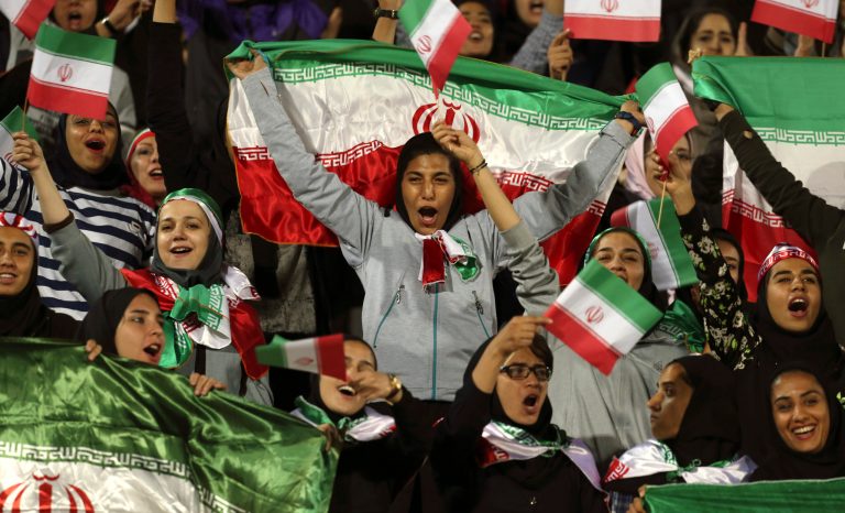 In this Oct. 16, 2018 photo, Iranian women cheer as they wave their country's flag after authorities in a rare move allowed a select group of women into Azadi stadium to watch a friendly soccer match between Iran and Bolivia, in Tehran, Iran. 