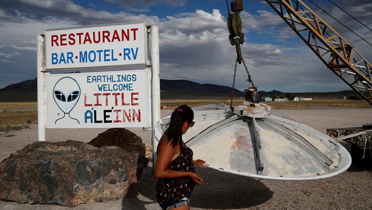 FILE - In this July 22, 2019 file photo, Grace Capati looks at a UFO display outside of the Little A'Le'Inn, in Rachel, Nev., the closest town to Area 51. The originator of the "Storm Area 51" internet hoax is citing concerns about organization and funding for withdrawing from an event called "Alienstock" scheduled next week in the remote Nevada desert. Matty Roberts said in interviews Tuesday, Sept. 10, 2019 in Las Vegas that he was worried events hosted by innkeeper Connie West in the tiny town of Rachel might not succeed. West told The Associated Press she has 22 musical and comedic acts booked and her Sept. 19-21 festival at the Little A'Le'Inn will go on.