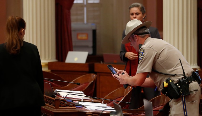 A California Highway Patrol Officer photographs a desk on the Senate floor after a red liquid was thrown from the Senate Gallery during the Senate session at the Capitol in Sacramento, California, on Friday. The Senate was cleared as an investigation is taking place. Authorities took a person into custody.