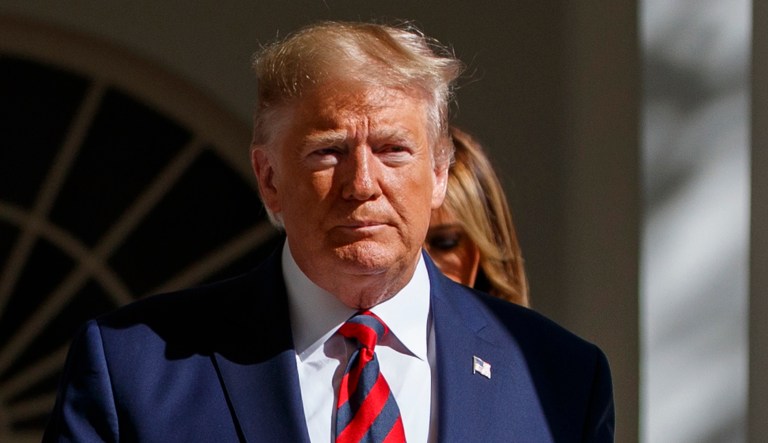 President Trump walks near the White House. His wife, Melania, walks behind him.
