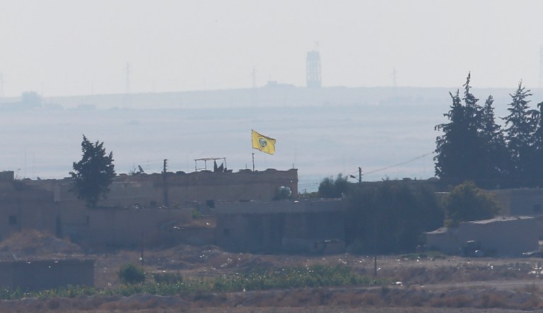 In this photo taken from the Turkish side of the border between Turkey and Syria, in Akcakale, Sanliurfa province, southeastern Turkey, a flag of Kurdish People's Protection Units, or YPG, flies on a building in the Syrian town of Tel Abyad, Tuesday, Oct. 8, 2019. 