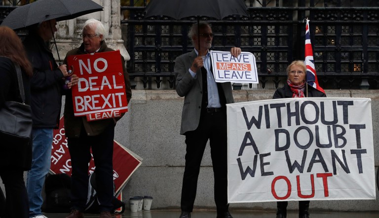 Pro-Brexit campaigners stand under umbrellas with their placards outside the Houses of Parliament in London, Monday, Oct. 21, 2019. The European Commission says the fact that British Prime Minister Boris Johnson did not sign a letter requesting a three-month extension of the Brexit deadline has no impact on whether it is valid and that the European Union is considering the request.