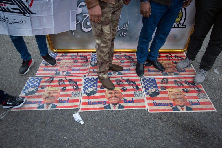 Mourners step over a U.S. flags with pictures of President Trump while waiting for the funeral of Iran's top general Qassem Soleimani and Abu Mahdi al-Muhandis, deputy commander of Iran-backed militias in Iraq known as the Popular Mobilization Forces, in Baghdad, Iraq, Saturday.