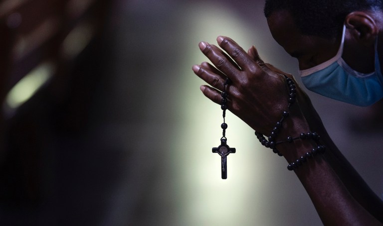 With rosary beads wrapped around clasped hands, a man bows in prayer during a Mass at the Metropolitan Cathedral, in Rio de Janeiro, Brazil, Saturday, July 4, 2020. Following an easing of restrictions related to COVID-19, the Catholic church in Rio celebrated its first Mass with 30% of its worshippers, while observing preventive measures to avoid spreading the new coronavirus. (AP Photo/Leo Correa)
