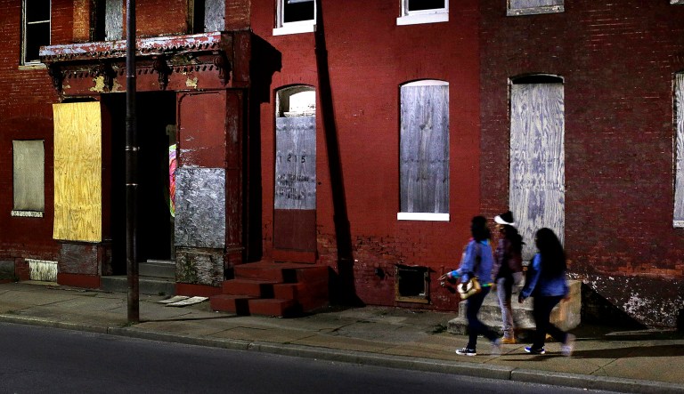 Women walk past blighted row houses in Baltimore.