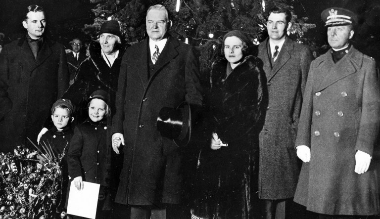 U.S. President Herbert Hoover, third from left, poses with his family at the Washington community Christmas tree after lighting the tree on Christmas Eve, Dec. 24, 1931. From left to right are, Allan Hoover, son; first lady Lou Henry Hoover; the President; daughter-in-law Margaret Hoover and her husband, Herbert Hoover Jr., and Colonel James A. Ulio, aid to the president.  The grandchildren are Herbert III, known as Pete, left, and Peggy Ann, holding the president's hand.