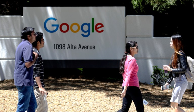 Pedestrians cross the street in front of a Google sign at the company's headquarters in Mountain View, Calif.
