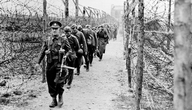 Led by a British soldier, a line of German prisoners of war is marched along a barbed-wire barricaded lane as they arrive at a POW camp somewhere in England in June 1944.