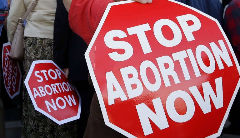 People carry anti-abortion signs saying "Stop Abortion Now."