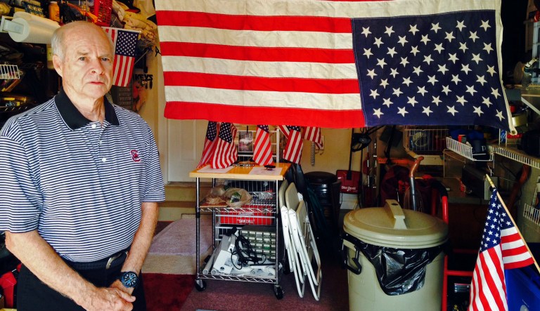 In this photo taken Wednesday, July 2, 2014, Larry Murphree, 73, stands in his garage next to an upside down American flag in Jacksonville, Fla. The U.S. Air Force veteran hangs the flag that way in protest of his condo association's decision to fine him for sticking a tiny flag in a flower pot on his porch. Homeowners are permitted to display a flag at The Tides Condominium at Sweetwater, but it must be in accord with specific rules. The flag violates the communityâs âflower pot ordinanceâ which says âcontents of planters are limited to maintained foliage,â court documents show. âTheyâve got to be stopped, and Iâm going to stop them,â he said. âIâve just dug in my heels.â