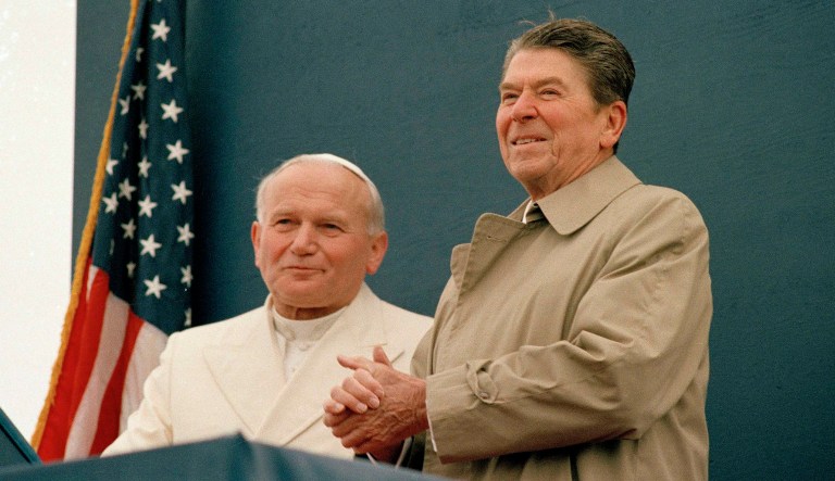 President Ronald Reagan smiles at the crowd as Pope John Paul II stands by his side during a joint appearance.