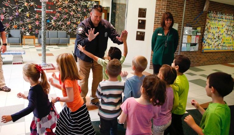 In this May 6, 2016, photo, Forest Dale Elementary School principal Deanna Pitman, right, and Carmel, (Ind.) police officer Greg DeWald welcome students as they return to the school following an intruder drill at the school in Carmel, Ind.