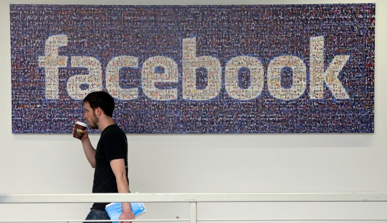 A Facebook employee walks past a sign at Facebook headquarters in Menlo Park, Calif.