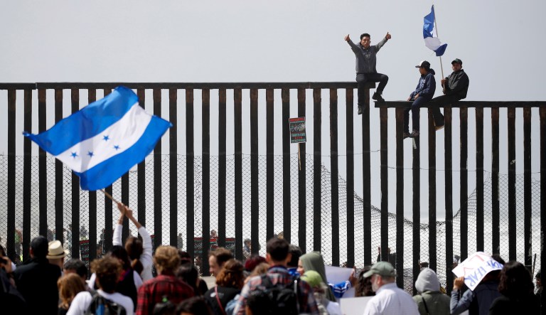 Central American migrants sit on top of the border wall on the beach in San Diego during a gathering of migrants living on both sides of the border, Sunday. 