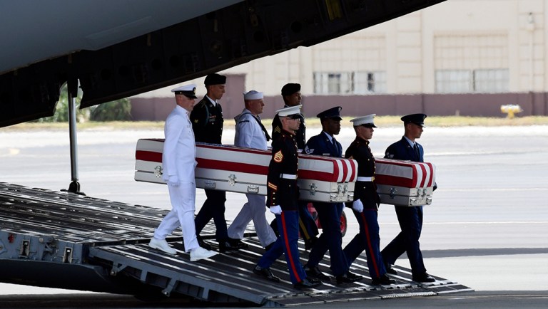 Military members carry transfer cases from a C-17 at a ceremony marking the arrival of the remains believed to be American service members who fell in the Korean War.