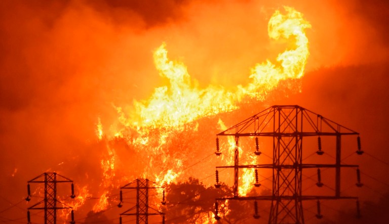 In this Dec. 16, 2017, file photo provided by the Santa Barbara County Fire Department, flames burn near power lines in Sycamore Canyon near West Mountain Drive in Montecito, Calif.