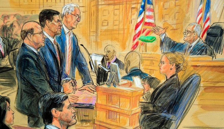 This courtroom sketch depicts President Trump's former national security adviser Michael Flynn, standing center, flanked by his lawyers, listening to U.S. District Judge Emmet Sullivan, right, as he addresses Flynn and points to the American flag inside the federal court in Washington, Washington, Tuesday, Dec. 18, 2018. Sullivan agreed to postpone Flynn's sentencing so he can continue cooperating with the Russia probe.