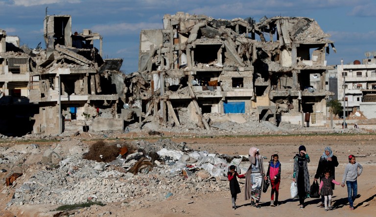 In this March 31, 2018 photo, Syrian citizens walk in front of buildings that were destroyed during the battle between the U.S.-backed Syrian Democratic Forces fighters and Islamic State militants, in Manbij, north Syria. On Friday, Dec. 28, 2018, Syriaâs military said it entered the flashpoint Kurdish-held town of Manbij, where Turkey has threatened an offensive, a claim that was refuted by U.S. troops who patrol the town. The announcement and the conflicting reports reflect the potential for chaos in the wake of the U.S. surprise decision to withdraw troops from Syria.