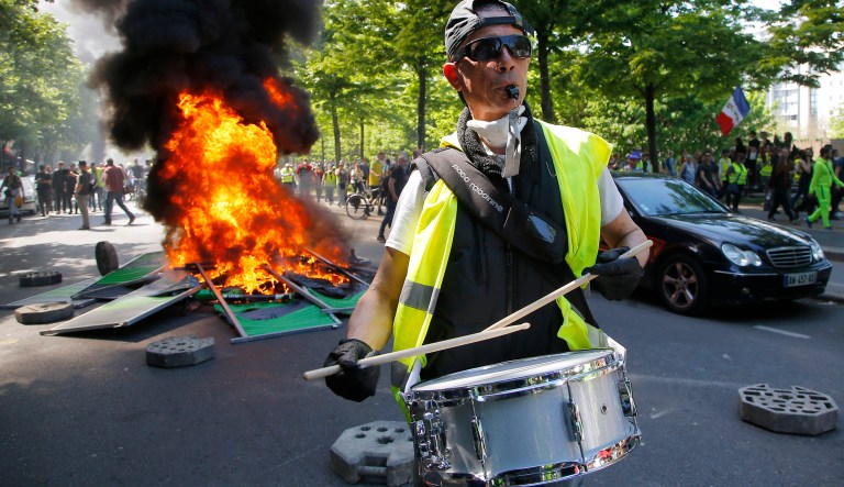 A man bangs a drum in front of a fire on the street during a yellow vest demonstration in Paris, Saturday, April 20, 2019.