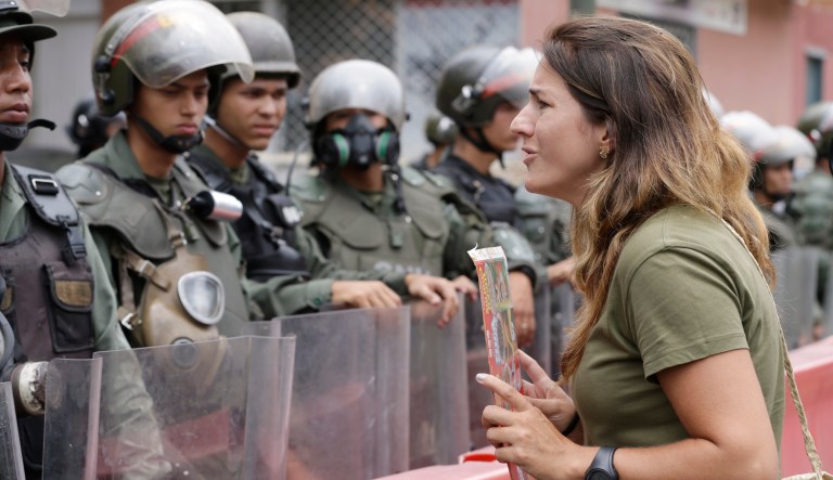 An opponent to Venezuela's President Nicolas Maduro faces riot police officers during a march in Caracas, Venezuela, Saturday, May 4, 2019. Opposition leader Juan Guaido took his quest to win over Venezuela's troops back to the streets, calling his supporters to participate in an outreach to soldiers outside military installations across the country.