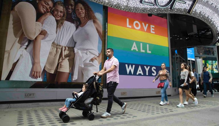 In this Thursday, June 20, 2019, people walk past a pride display at the Loft store in New York's Times Square. For Pride month, retailers across the country are selling goods and services celebrating LGBTQ culture. They range from Macyâs same-sex wedding registries to the Times Square digital billboards beaming apparel sold in shops below.
