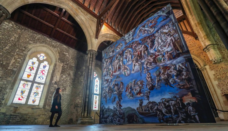A lady looks at the Last Judgement on display at a press view for the Michaelangelo's Sistine Chapel - A Different View exhibition at the Great Hall in Winchester. PRESS ASSOCIATION Photo. Picture date: Thursday July 4, 2019.  Officially licensed by the Vatican Museums, frescoes have been photographed and reproduced at high resolution and transferred to special fabric webs, allowing a true-to-life reproduction the ceiling and giving visitors a unique opportunity for a close-up view.