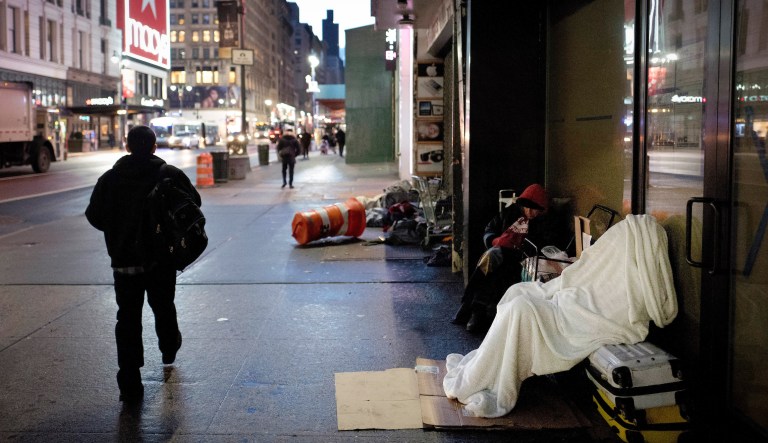 In this Jan. 11, 2017, file photo, a homeless person sleeps under a blanket while seated on a New York sidewalk.