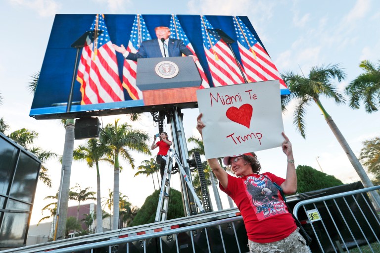 Maria Salazar, foreground, holds up a sign that says, "Miami loves you Trump," in Spanish as supporters watch President Donald Trump on a large screen in an overflow area outside the King Jesus International Ministry, during a January rally in Miami.