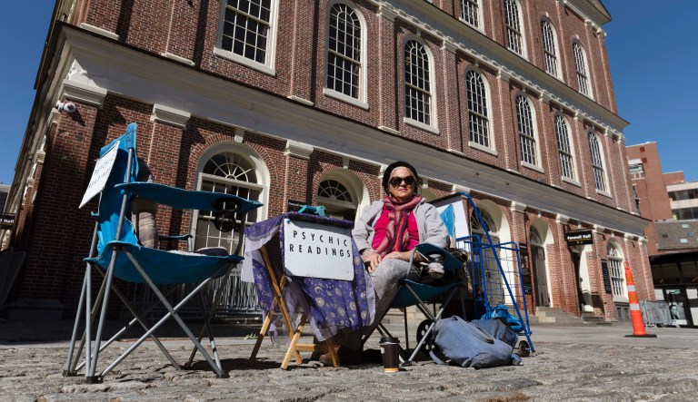 A fortune teller going by the name of Andrea wait for customers in front of Faneuil Hall in Boston, on a plaza that is usually busy with tourists, Saturday, March, 14, 2020.