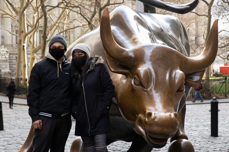 Constantinos Georgiou, left, and Kemi Njemanze wear masks as they pose with the Charging Bull, Monday, March 16, 2020 in New York's financial district. The couple visiting from Sydney, Australia said they wear the masks out of concern for COVID-19.