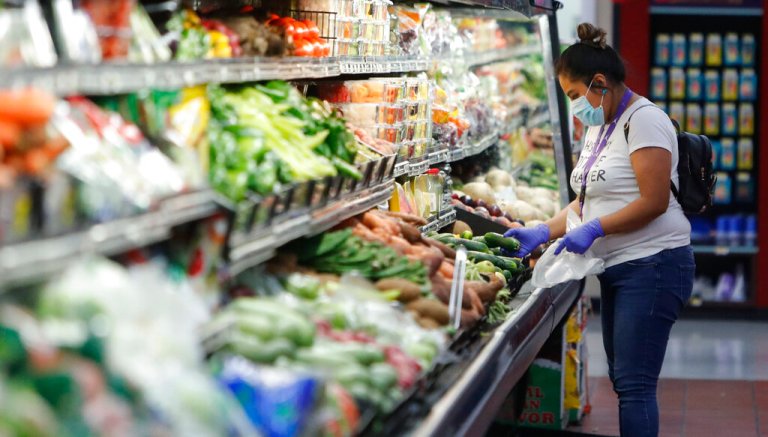A woman wears a mask amid social distancing during the COVID-19 outbreak while shopping the well stocked produce section at El Rancho grocery store in Dallas, Thursday, March 26, 2020.