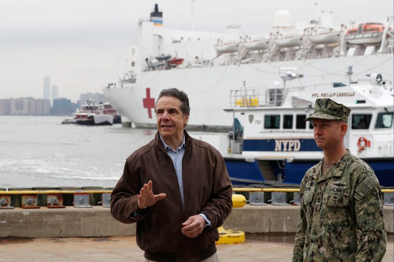 New York Gov. Andrew Cuomo, left, gestures during a brief news conference as he stands beside a Rear Adm. John B. Mustin as the USNS Comfort, a naval hospital ship with a 1,000 bed-capacity, pulls into Pier 90 Monday, March 30, 2020, in New York. The ship will be used to treat New Yorkers who don't have coronavirus as land-based hospitals fill up with and treat those who do.