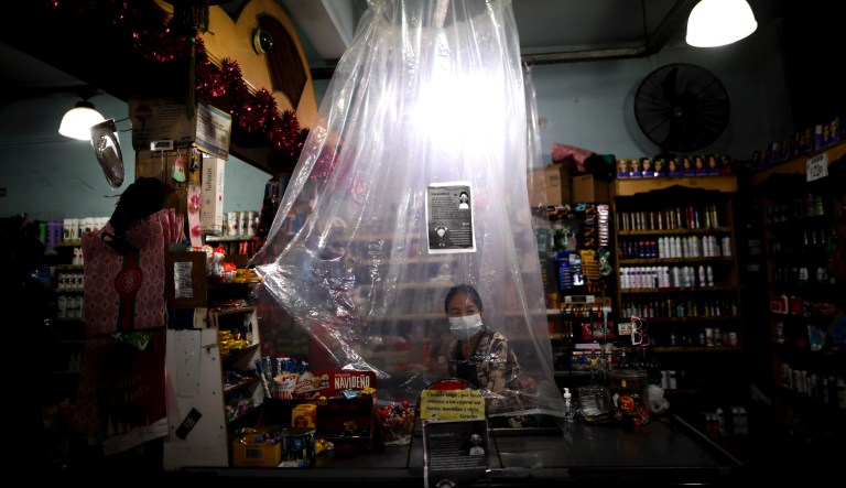 In this March 16, 2020, file photo, supermarket cashier waits for costumers behind a makeshift plastic curtain as a precaution against the spread of the new coronavirus, in Buenos Aires, Argentina. Grocery workers across the globe are working the front lines during lockdowns meant to keep the coronavirus from spreading.