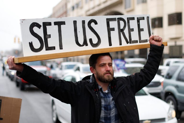 Steve Polet holds a sign during a protest at the State Capitol in Lansing, Mich., Wednesday, April 15, 2020. Flag-waving, honking protesters drove past the Michigan Capitol on Wednesday to show their displeasure with Michigan Gov. Gretchen Whitmer's orders to keep people at home and businesses locked during the new coronavirus COVID-19 outbreak.