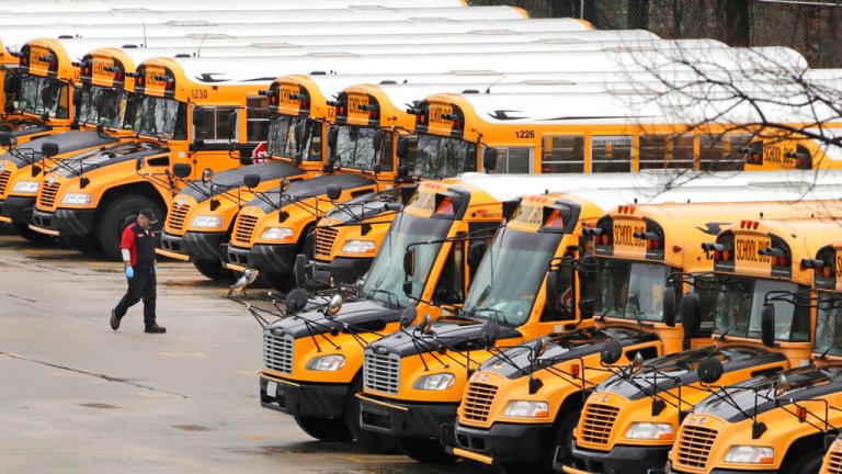 A worker passes public school buses parked at a depot in Manchester, N.H., Monday, April 27, 2020. 