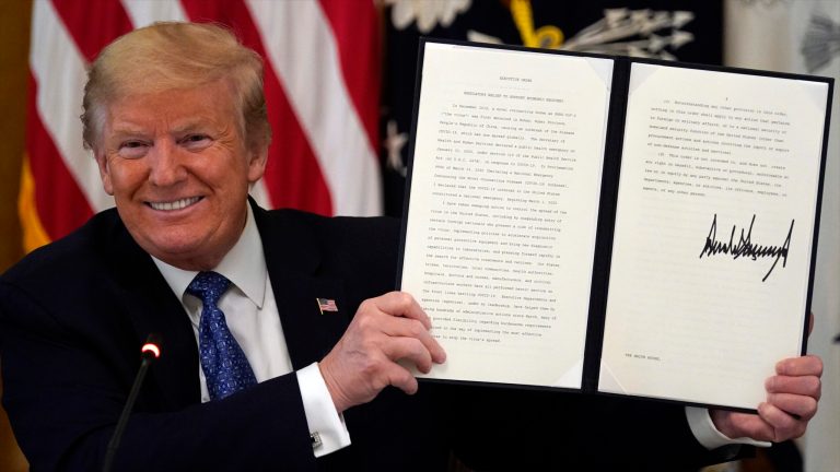 President Trump holds up a signed executive order limiting regulations to support economic recovery during a Cabinet Meeting in the East Room of the White House, Tuesday, May 19, 2020, in Washington.