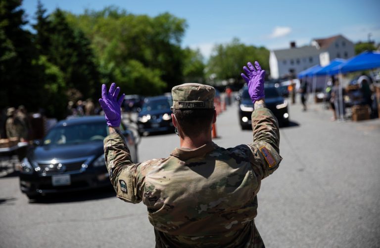 A member of the Rhode Island National Guard directs motorists as volunteers with the Dairy Farmers of America distribute free milk to families in need, Wednesday, May 27, 2020, in Pawtucket, R.I. Governors want to extend the use of the Guard through the reopening.