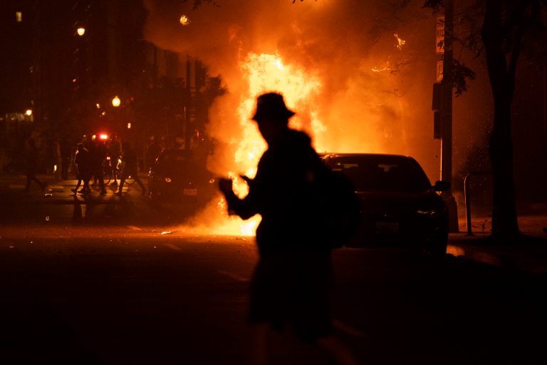 A demonstrator watches a car burn during a protest over the death of George Floyd, Sunday. Protesters targeted a Fox crew.