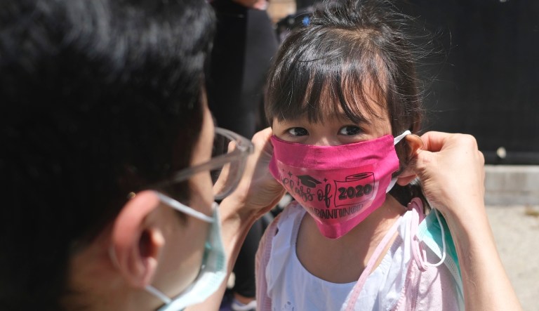 In this June 10, 2020, file photo, Olivia Chan's father helps her with a new mask she received during a graduation ceremony for her Pre-K class in front of Bradford School in Jersey City, N.J.