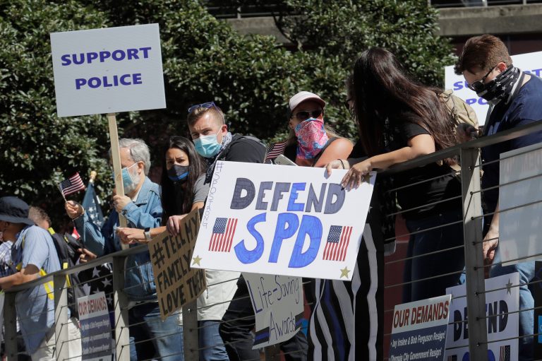 People hold signs as they take part in a rally in support of police and other law enforcement officers, Wednesday, July 15, 2020, in front of City Hall in Seattle. More Americans are voicing opposition to defunding police departments.