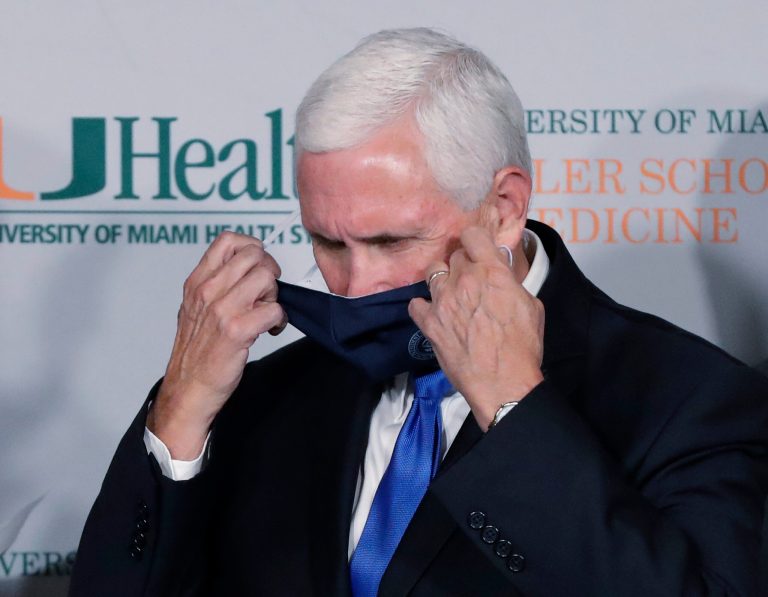 Vice President Mike Pence takes off his mask before speaking during a news conference at the University of Miami Miller School of Medicine Don Soffer Clinical Research Center, Monday in Miami. Pence was in Florida to mark the beginning of Phase III trials for a coronavirus vaccine.