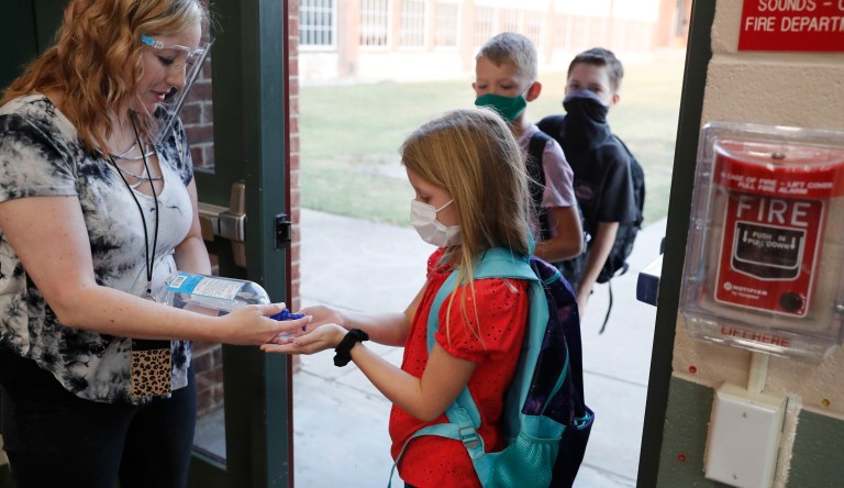 In this Aug. 5, 2020, file photo, wearing masks to prevent the spread of COVID19, elementary school students use hand sanitizer before entering school for classes in Godley, Texas. As schools reopen around the country, their ability to quickly identify and contain coronavirus outbreaks before they get out of hand is about to be put to the test.