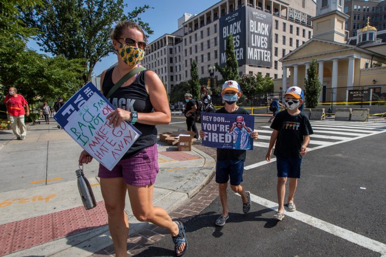 A mother and her children hold their placards as they walk to visit the Black Lives Matter Plaza near the White House in Washington, and join other marchers during the March on Washington, Friday, Aug. 28, 2020, commemorating the 57th anniversary of the Rev. Martin Luther King Jr.'s "I Have A Dream" speech. 