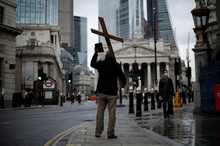 A man holding a cross and a Bible preaches about Christianity, backdropped by the Royal Exchange and the Bank of England during England's second coronavirus lockdown, Wednesday, Nov. 18, 2020. For the first time ever, Christians in England and Wales now constitute a minority. 