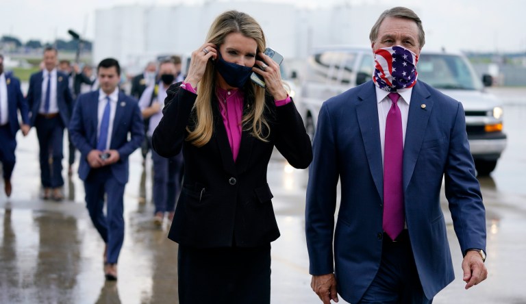 Kelly Loeffler puts on a face mask as she walks with David Perdue at UPS Hapeville Airport Hub in Atlanta. 